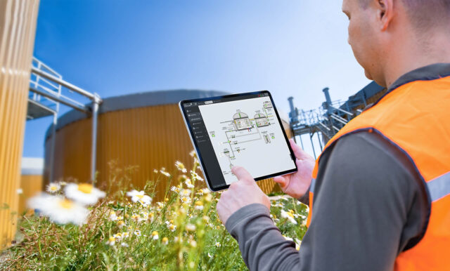Een persoon houdt een tablet vast voor een industriële installatie buiten.