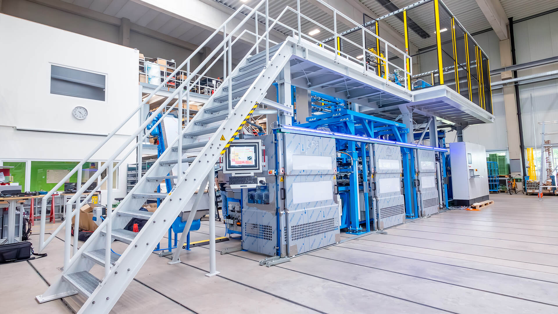 Moderne industriële installatie met trapopgang, geautomatiseerde machines en productiegebieden in een lichte fabriekshal.