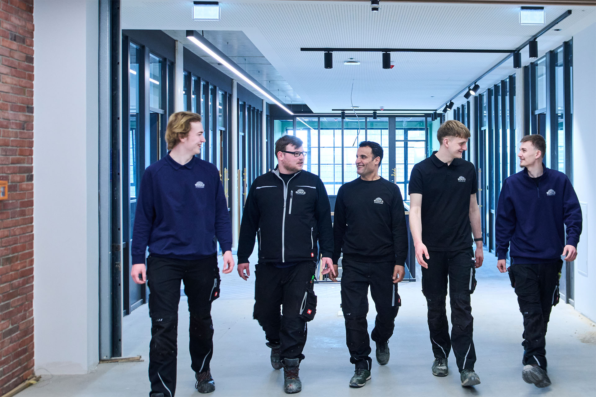 Vijf medewerkers in SCHULZ-kleding lopen door een gang.